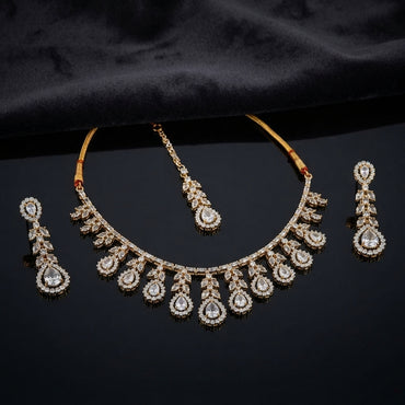 Gold CZ Pear Fringe Necklace Maang Tikka and Linear Drop Earrings Bridal Set — 22K gold-tone 3-piece bridal set with graduating pear CZ halo fringe necklace with marquise leaf clusters and traditional red thread spine matching maang tikka with pear CZ halo drop and 3-tier linear drop earrings displayed on dark black satin surface with mirror reflection