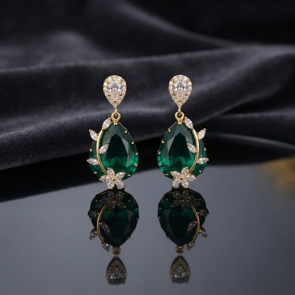 Gold CZ Pear Halo and Marquise Floral Vine Oval Crystal Drop Earrings in Emerald Green on dark charcoal slate satin with dark mirror surface showing 22K gold-tone pair with pear white CZ halo stud deep vivid emerald green faceted oval crystal pendant marquise CZ floral vine sprigs on both sides and 5-petal marquise CZ daisy flower base
