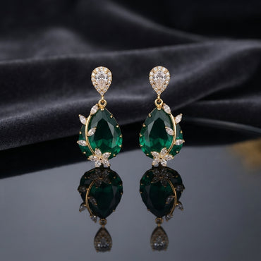 Gold CZ Pear Halo and Marquise Floral Vine Oval Crystal Drop Earrings in Emerald Green on dark charcoal slate satin with dark mirror surface showing 22K gold-tone pair with pear white CZ halo stud deep vivid emerald green faceted oval crystal pendant marquise CZ floral vine sprigs on both sides and 5-petal marquise CZ daisy flower base