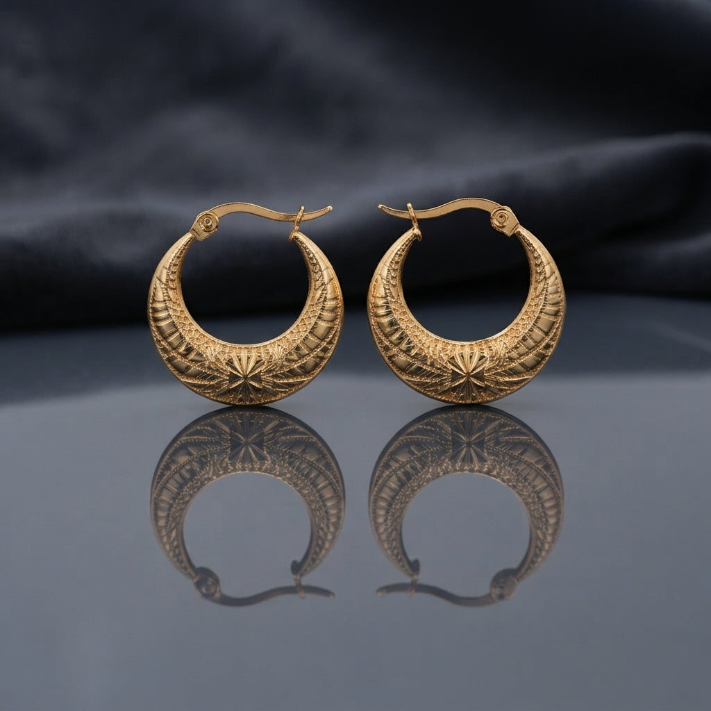 Gold Diamond-Cut Engraved Starburst Crescent Basket Hoop Earrings pair standing upright on dark mirror surface with charcoal slate satin backdrop showing 22K antique gold-tone wide crescent basket hoops with intricate diamond-cut engraved front face featuring parallel hatching upper half and twin 8-pointed starburst medallion engravings lower half with sharp mirror reflection below