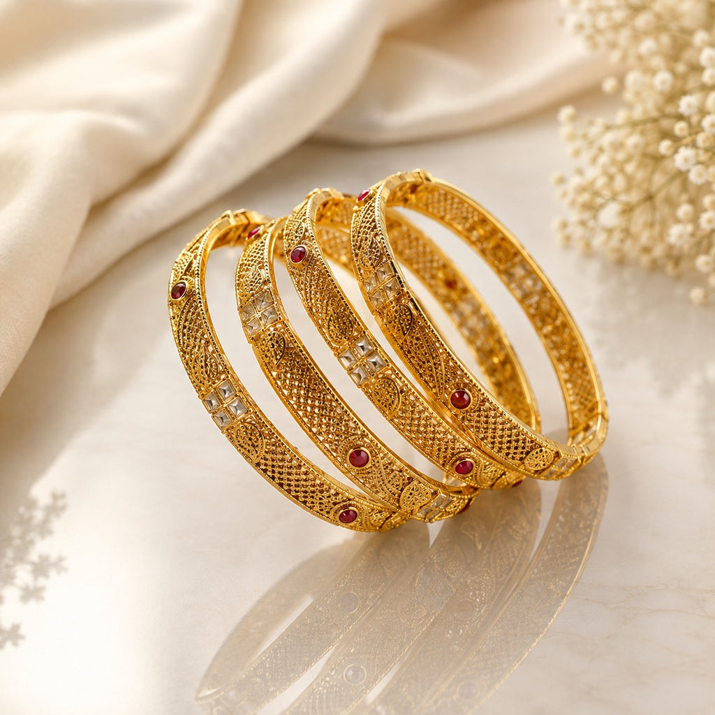 Gold-Tone Diamond Lattice Filigree Ruby & White CZ Bangle Set of 4 stacked on cream marble surface with ivory silk fabric and baby's breath flowers backdrop