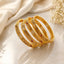 Gold-Tone Diamond Lattice Filigree Ruby & White CZ Bangle Set of 4 stacked on cream marble surface with ivory silk fabric and baby's breath flowers backdrop