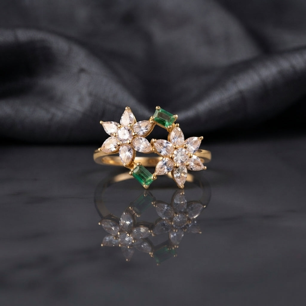 Gold Double Flower Cluster CZ Cocktail Ring in deep vivid emerald green CZ accent variant — luxury flat-lay on mirror surface with charcoal silk backdrop