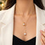 Gold Double Pearl Circle Lariat Y-Necklace close-up worn by model in white blazer and black top with gold bokeh backdrop