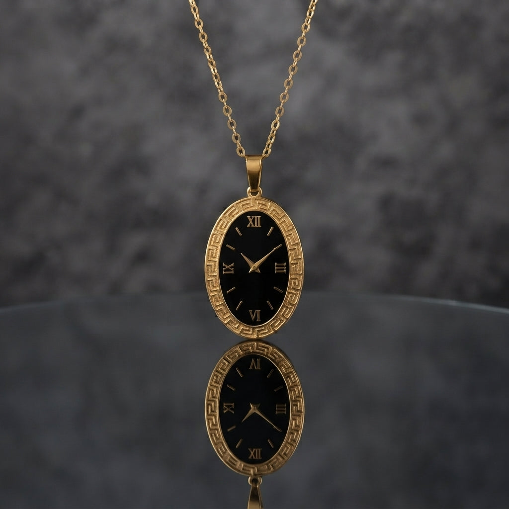 Gold Elongated Oval Greek Key Black Dial Watch-Face Pendant Necklace in 18K gold-tone PVD stainless steel on dark grey mirror surface with grey textured backdrop showing tall portrait oval pendant with continuous Greek key meander engraved border and deep black decorative Roman numeral watch-face dial sticker with gold-tone hands on slim gold cable chain with mirror reflection below