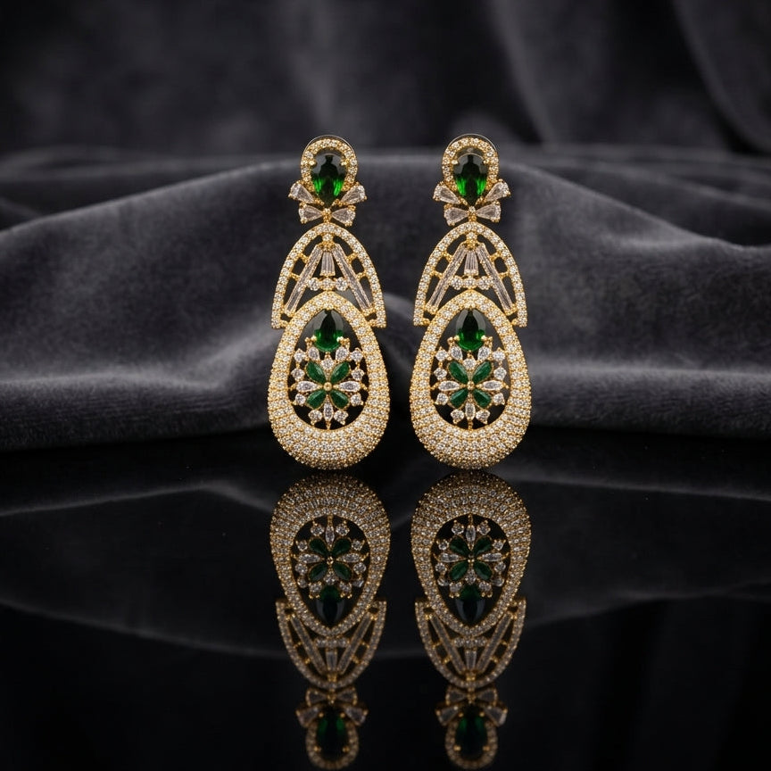 Gold Emerald Green CZ Art Deco Teardrop and Marquise Floral Starburst Drop Earrings — 18-22K gold-tone statement bridal earrings with oval emerald CZ micro-pavé disc stud baguette CZ bow connector open arch upper section and large open teardrop body with dense CZ micro-pavé frame and 6-petal marquise emerald CZ floral starburst interior displayed on dark black mirror surface with charcoal satin backdrop