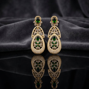 Gold Emerald Green CZ Art Deco Teardrop and Marquise Floral Starburst Drop Earrings — 18-22K gold-tone statement bridal earrings with oval emerald CZ micro-pavé disc stud baguette CZ bow connector open arch upper section and large open teardrop body with dense CZ micro-pavé frame and 6-petal marquise emerald CZ floral starburst interior displayed on dark black mirror surface with charcoal satin backdrop
