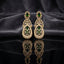 Gold Emerald Green CZ Art Deco Teardrop and Marquise Floral Starburst Drop Earrings — 18-22K gold-tone statement bridal earrings with oval emerald CZ micro-pavé disc stud baguette CZ bow connector open arch upper section and large open teardrop body with dense CZ micro-pavé frame and 6-petal marquise emerald CZ floral starburst interior displayed on dark black mirror surface with charcoal satin backdrop