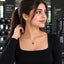 Gold Emerald Rectangle CZ Halo Pendant Necklace worn by model in black long-sleeve top at gym setting with dumbbell rack backdrop