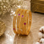 Gold-Tone Filigree Granule Bangle Set of 4 with alternating Ruby Red & White CZ square accents on marble surface with baby's breath flowers and antique gold box