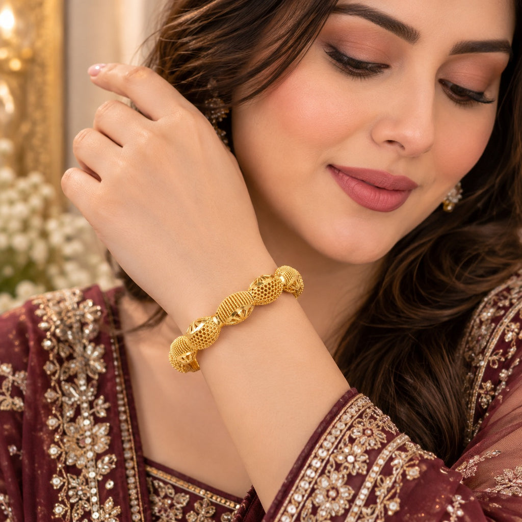 Gold Filigree Mesh Starburst Oval Bead Kangan Bangle Set Pair of 2 worn on wrist of Pakistani female model in deep burgundy heavily embroidered formal suit with gold zardozi threadwork in luxury gold chandelier backdrop with white gypsophila flowers showing antique gold-tone filigree mesh oval bead kangan bangles on wrist
