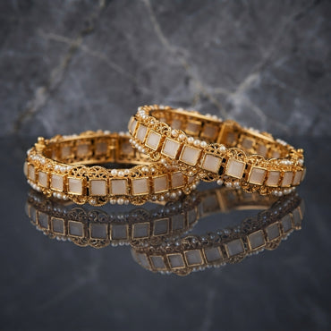 Gold Filigree Square Stone Seed Pearl Bangles Bridal Pair in 18K antique gold-tone plating on dark grey mirror surface with marble backdrop showing two rigid bangles with alternating square white ivory stone tiles in gold box-bezel settings and ornate gold filigree scroll medallions with seed pearl bead top and bottom edges and mirror reflection below