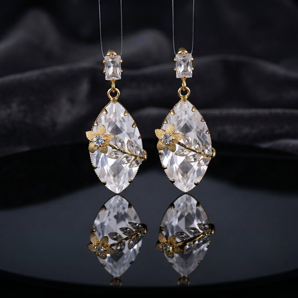 Gold Floral CZ Leaf Crystal Gem Drop Earrings in Emerald Green showing pair suspended on monofilament wire against dark burgundy velvet backdrop with baguette CZ stud top large faceted diamond-shape emerald green crystal drop with gold daisy flower and marquise CZ leaf sprig overlay and mirror reflection below