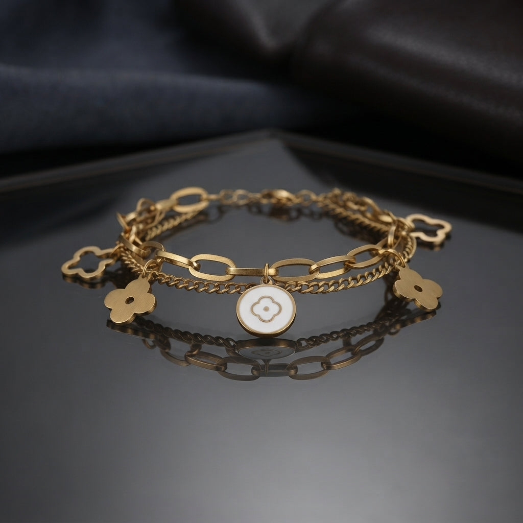 Gold Four-Leaf Clover Charm Double Layer Chain Bracelet in 18K gold-tone PVD stainless steel on dark grey mirror surface with dark silk backdrop showing bold oval paperclip link chain layered with fine curb chain featuring 4 open-cut gold four-leaf clover outline charms and 1 white enamel round medallion centre charm with raised gold quatrefoil motif with mirror reflection below