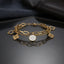 Gold Four-Leaf Clover Charm Double Layer Chain Bracelet in 18K gold-tone PVD stainless steel on dark grey mirror surface with dark silk backdrop showing bold oval paperclip link chain layered with fine curb chain featuring 4 open-cut gold four-leaf clover outline charms and 1 white enamel round medallion centre charm with raised gold quatrefoil motif with mirror reflection below