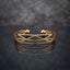 Gold Geometric Wireframe Diamond Lattice Open Cuff Bangle in 18K gold-tone PVD stainless steel on dark mirror surface with grey bokeh backdrop showing wide open C-shape cuff with repeating diamond rhombus X-cross geometric lattice wireframe pattern and two smooth gold ball bead finials at open ends with mirror reflection below
