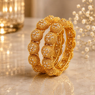 Gold-Tone Granule Dome Ball Cluster & White CZ Polki Flower Bangle Set of 2 on cream marble surface with gold candle lantern and baby's breath flowers backdrop
