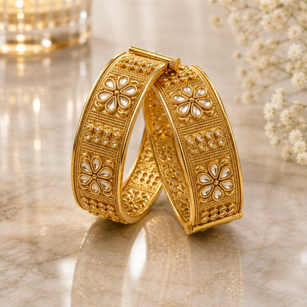 Gold-Tone Wide Granule Kundan Polki Five-Petal Flower Panel Kada Bangle Set of 2 leaning on gold marble surface with crystal candle holder and baby's breath flowers backdrop