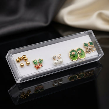 Gold Green Tulip Oval Floral Pearl Clover 5-Pair Stud Earring Set displayed in open clear acrylic gift box on black mirror surface with grey and cream fabric backdrop showing all five pairs on white velvet insert with mirror reflection below