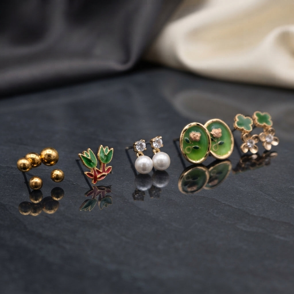 Gold Green Tulip Oval Floral Pearl Clover 5-Pair Stud Earring Set flat lay on dark black stone surface with grey and cream fabric backdrop showing gold ball arc studs green tulip enamel studs with red coral stem white CZ pearl drop studs large green oval enamel stud with pink rose and gold bead border and green clover blush CZ flower cluster stud with mirror reflections below