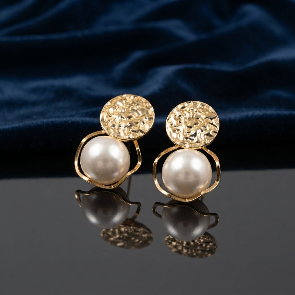 Gold Hammered Disc and Floating Pearl Open Orbit Drop Earrings pair standing on dark grey mirror surface with deep navy blue velvet backdrop showing 18K warm yellow gold-tone hammered textured disc top with short wire connector and open circular orbit frame cradling large floating white simulated pearl with mirror reflection below