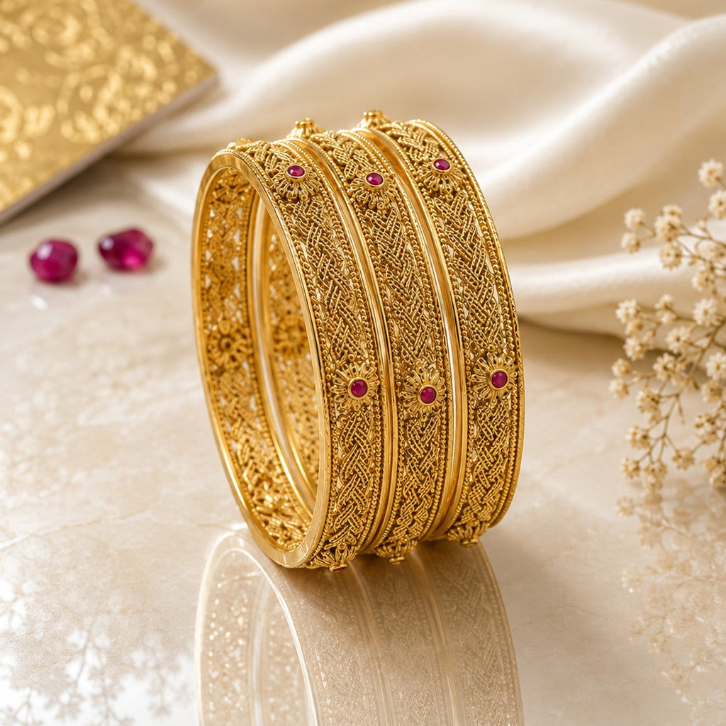 Gold-Tone Herringbone Filigree & Ruby CZ Sunflower Bangle Set of 4 stacked on cream marble surface with white silk fabric, ruby gemstones and baby's breath flowers backdrop