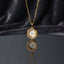 Gold Hexagon Greek Key Watch-Face Pendant Necklace in 18K gold-tone PVD stainless steel on dark grey mirror surface with dark silk backdrop showing bold hexagon pendant with continuous Greek key meander engraved border and decorative white Roman numeral watch-face dial sticker on slim gold cable chain with mirror reflection below