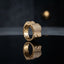 Gold Iced Out CZ Micro-Pavé Wide Band Filigree Statement Ring — 22K gold-tone wide luxury band ring with fully iced out dense round white CZ micro-pavé raised square top and open sunburst geometric filigree cutout inner band, dramatic dark mirror surface with spotlight backdrop editorial