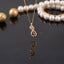 Gold Infinity Heart Rose CZ Pendant Necklace in 18K gold-tone plating on dark grey mirror surface with pearl bracelet and gold sphere backdrop showing delicate fine cable chain with 3D sculptural infinity heart rose pendant featuring micro-pave white CZ diagonal row blooming rose top and open heart base loop with mirror reflection below