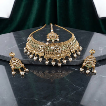 Gold Kundan Meenakari Pearl Drop Choker Necklace Earrings & Maang Tikka Bridal Set on dark grey marble surface with green velvet drape backdrop