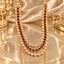 Gold-Tone Kundan Polki & Ruby Red CZ Alternating Oval Bezel 4-Strand Layered Bridal Statement Necklace on gold satin surface with bokeh gold lights and white floral accents in luxury editorial setting