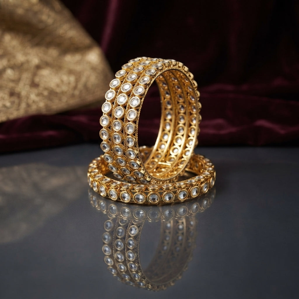 Gold Kundan Round Polki Stone Wide Bangle Set of 4 standing upright on dark grey mirror surface with burgundy velvet and gold embroidered fabric backdrop showing four matching wide bangles with three rows of round kundan polki flat-cut CZ stones in gold-tone bezel settings and filigree granulation back with mirror reflection below