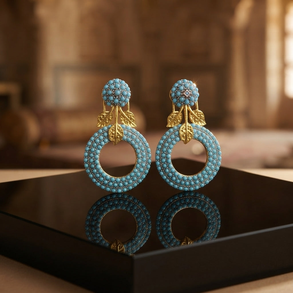 Gold Leaf CZ Pavé Circle Drop Earrings in Multi Color in 18K gold-tone plating on grey mirror surface with warm Mughal palace backdrop showing round dome ball stud top and large open circle drop fully covered in dense multi-color micro-pavé CZ stones in ruby red emerald green sapphire blue and white CZ with gold leaf connector and mirror reflection below