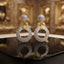 Gold Leaf CZ Pavé Circle Drop Earrings in White Diamond CZ in 18K gold-tone plating on dark black mirror tray surface with luxury gold interior backdrop showing round dome ball stud top and large open circle drop fully covered in dense white diamond CZ micro-pavé stones with gold leaf connector and mirror reflection below