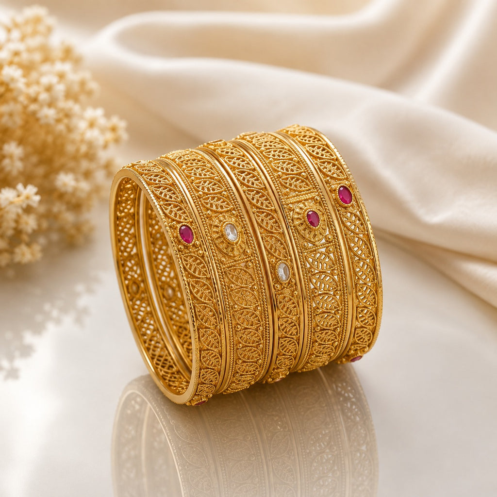 Gold-Tone Leaf Paisley Filigree Openwork Ruby & White CZ Bangle Set of 4 stacked on cream marble surface with ivory silk fabric and dried flower stems backdrop