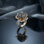 Gold Lotus Flower Cluster CZ Dome Cocktail Ring in Black — 22K gold-tone lotus flower basket ring with dense jet black CZ dome cluster crown, white CZ pavé petal halo, and split pavé shank, on dark mirror surface with charcoal silk backdrop