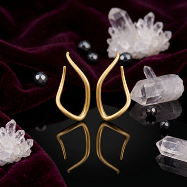 Gold-Tone Matte Sculptural Tulip Flame Open Teardrop Wishbone Long Drop Earrings on black mirror surface with white crystal quartz clusters, black hematite beads and deep burgundy velvet backdrop