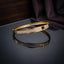 Gold Micro Pave CZ Geometric Panel Rigid Bangle on dark grey mirror surface with dark purple silk fabric backdrop showing 18K gold-tone polished oval rigid bangle with three rectangular micro-pave white round CZ panels and angular geometric gold notch dividers with mirror reflection below