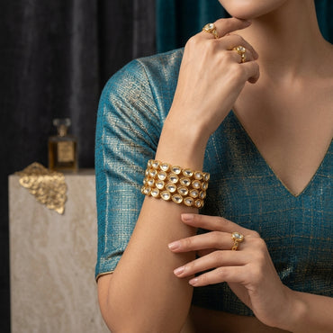 Gold Mixed-Shape Kundan Polki Teardrop Oval Full-Bezel Slim Bangle Set of 4 worn stacked on model wrist in teal tissue silk blouse with marble and dark backdrop showing wide cuff stack of four slim bangles with alternating teardrop and oval flat-cut CZ kundan polki stones in antique gold bezel settings