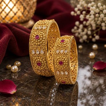 Gold-Tone Mughal Granule Polki & Ruby CZ Wide Kada Bangle Set of 2 on dark marble surface with gold lantern, rose petals, pearls and baby's breath flowers backdrop