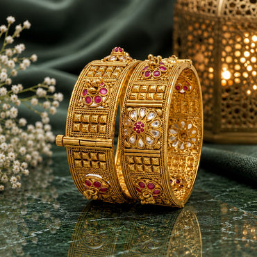 Gold-Tone Mughal Kundan Polki Flower & Ruby CZ Grid Panel Wide Kada Bangle Set of 2 on green marble surface with gold lantern and baby's breath flowers backdrop