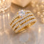 Gold-Tone Multi-Row Pavé White CZ Eternity Stack & Round Solitaire Bridal Ring Set on marble surface with gold crystal candle holder and baby's breath flowers backdrop