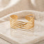 Gold Multi-Wire Crossover Open Cuff Bangle on white marble tile with cream linen drape backdrop