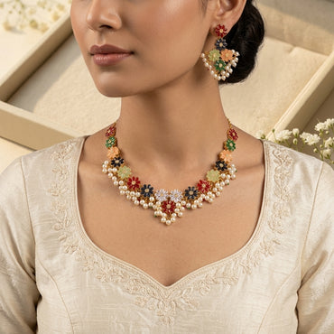 Gold Multicolor Enamel Daisy Flower Pearl Cluster Choker Necklace Earrings Set product flat lay on dark grey mirror surface with blue silk backdrop showing V-bib choker and matching earrings with multicolor enamel daisies and pearl clusters