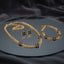 Gold Navy Blue Enamel 4-Leaf Clover Cuban Chain Necklace Bracelet Earrings Set — 3-piece matching set of heavy 22K gold-tone Cuban curb chain necklace with navy blue enamel 4-leaf clover charms, matching bracelet and clover stud earrings, luxury flat-lay on round mirror tray with dark charcoal silk backdrop