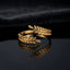 Gold Olive Laurel Leaf Wrap Bypass Adjustable Ring flat lay on dark black mirror surface with dark charcoal navy satin backdrop showing 18K gold-tone open wrap bypass ring with two detailed olive laurel leaf branches with individually raised engraved oval leaves crossing in graceful wrap design with mirror reflection below