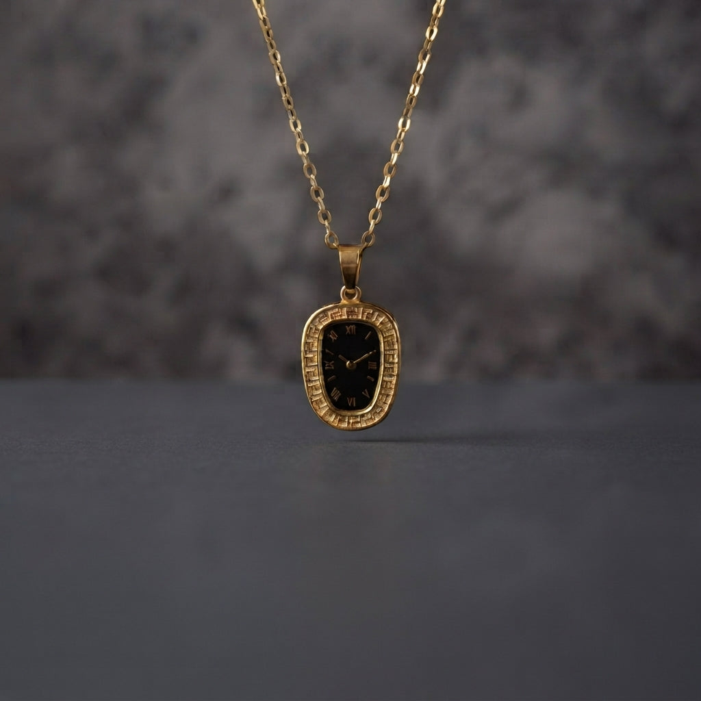 Gold Oval Greek Key Black Dial Watch-Face Pendant Necklace in 18K gold-tone PVD stainless steel hanging on grey marble textured backdrop showing rounded rectangle oval cushion pendant with continuous Greek key meander engraved border and decorative black Roman numeral watch-face dial sticker with gold-tone hands on slim gold cable paperclip link chain