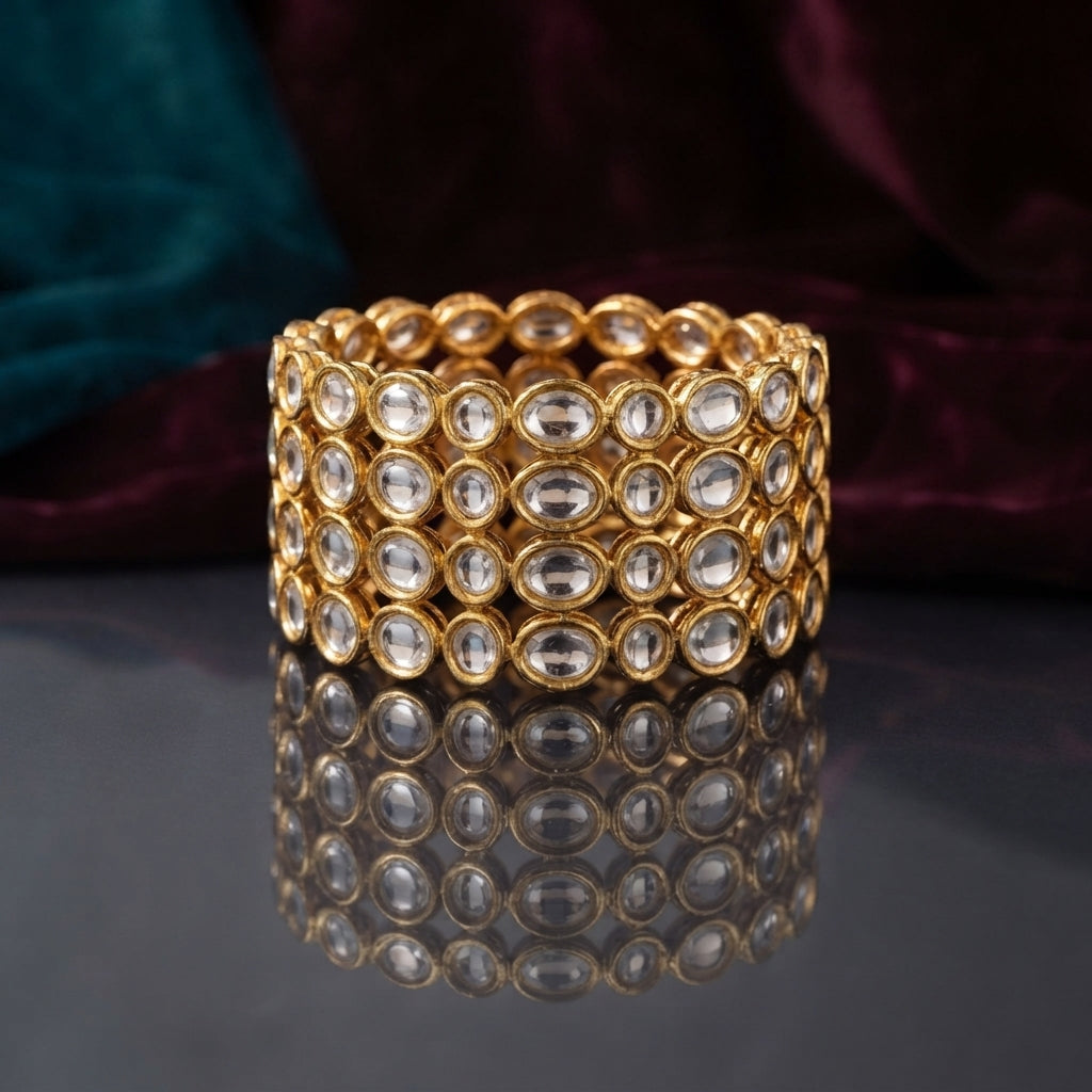Gold Oval Kundan Polki Full-Bezel Slim Bangle Set of 4 detail shot stacked on dark grey mirror surface with teal and burgundy velvet backdrop showing close up of continuous oval flat-cut CZ kundan polki stones in antique gold bezel settings all around four slim gold bangles with mirror reflection below