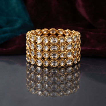 Gold Oval Kundan Polki Full-Bezel Slim Bangle Set of 4 detail shot stacked on dark grey mirror surface with teal and burgundy velvet backdrop showing close up of continuous oval flat-cut CZ kundan polki stones in antique gold bezel settings all around four slim gold bangles with mirror reflection below
