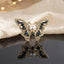 Gold Pearl Butterfly Crystal Brooch in Navy Blue on dark grey mirror surface with cream fabric and warm bokeh backdrop showing large butterfly brooch with open filigree gold wings dense micro-pave white CZ border navy blue marquise crystal wing stones and large faux pearl centre with mirror reflection below